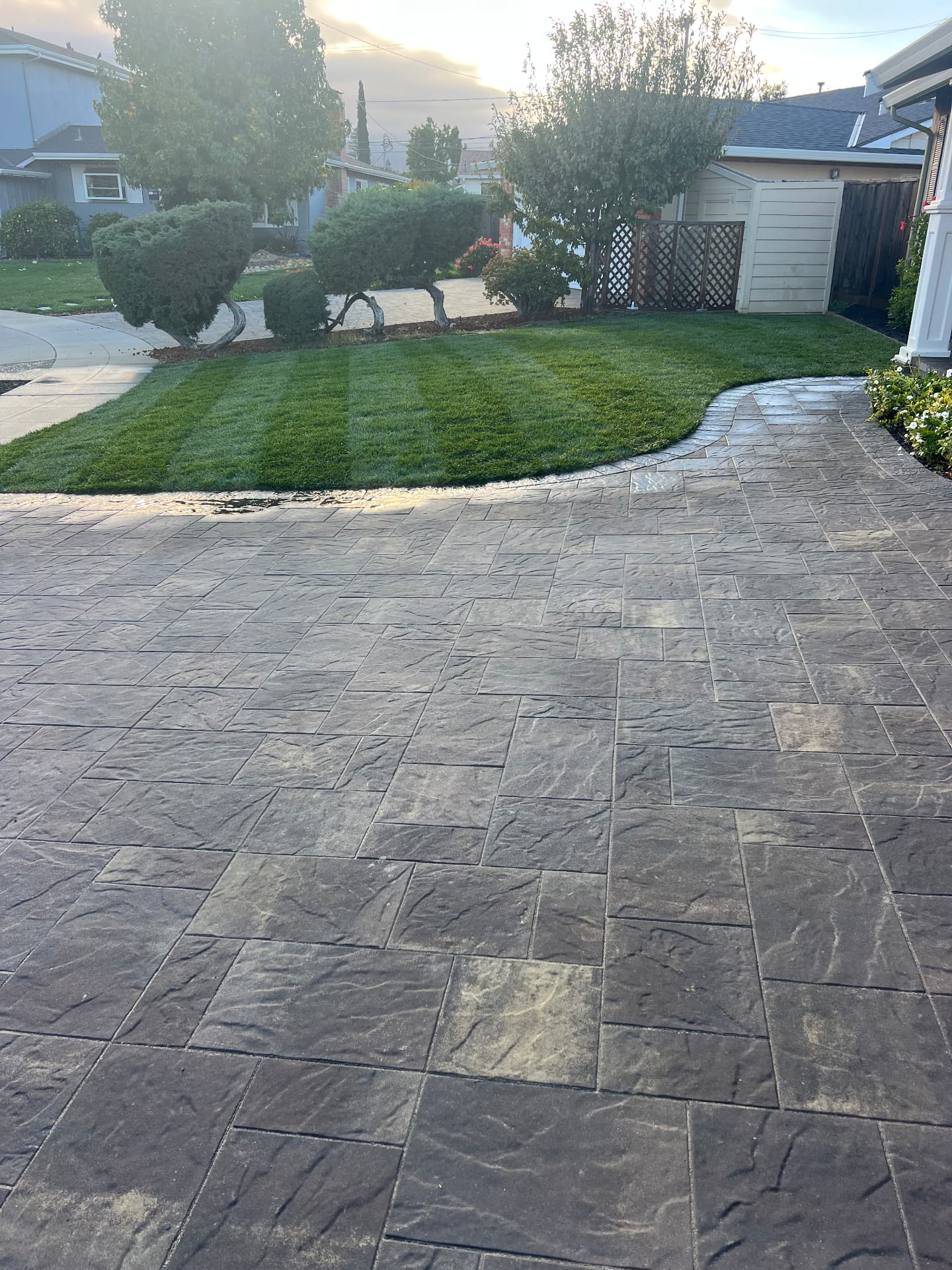 Charcoal paver driveway bordered by a striped lawn