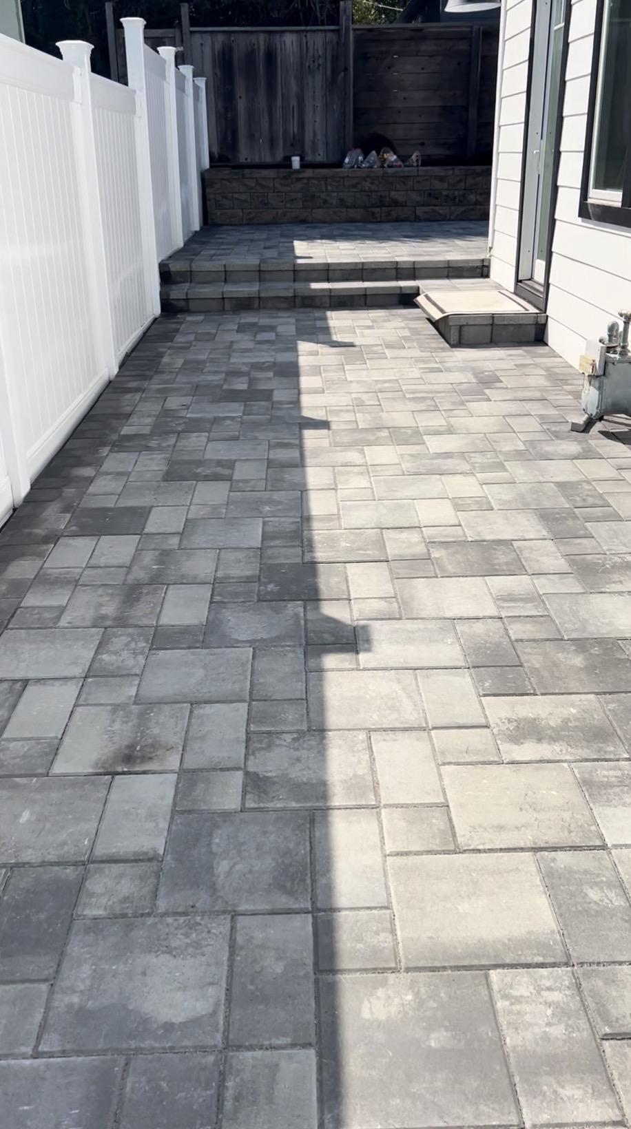 Paver patio and steps beside a white fence